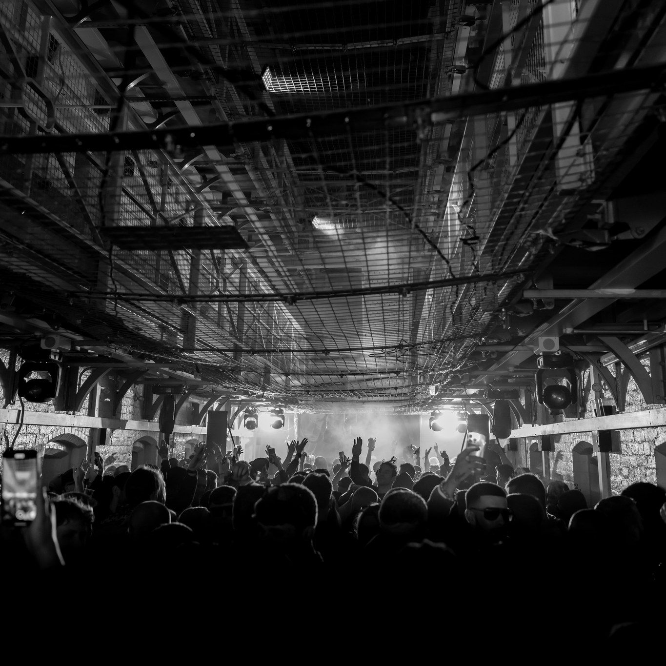 B&W crowd in prison wing with hands in the air